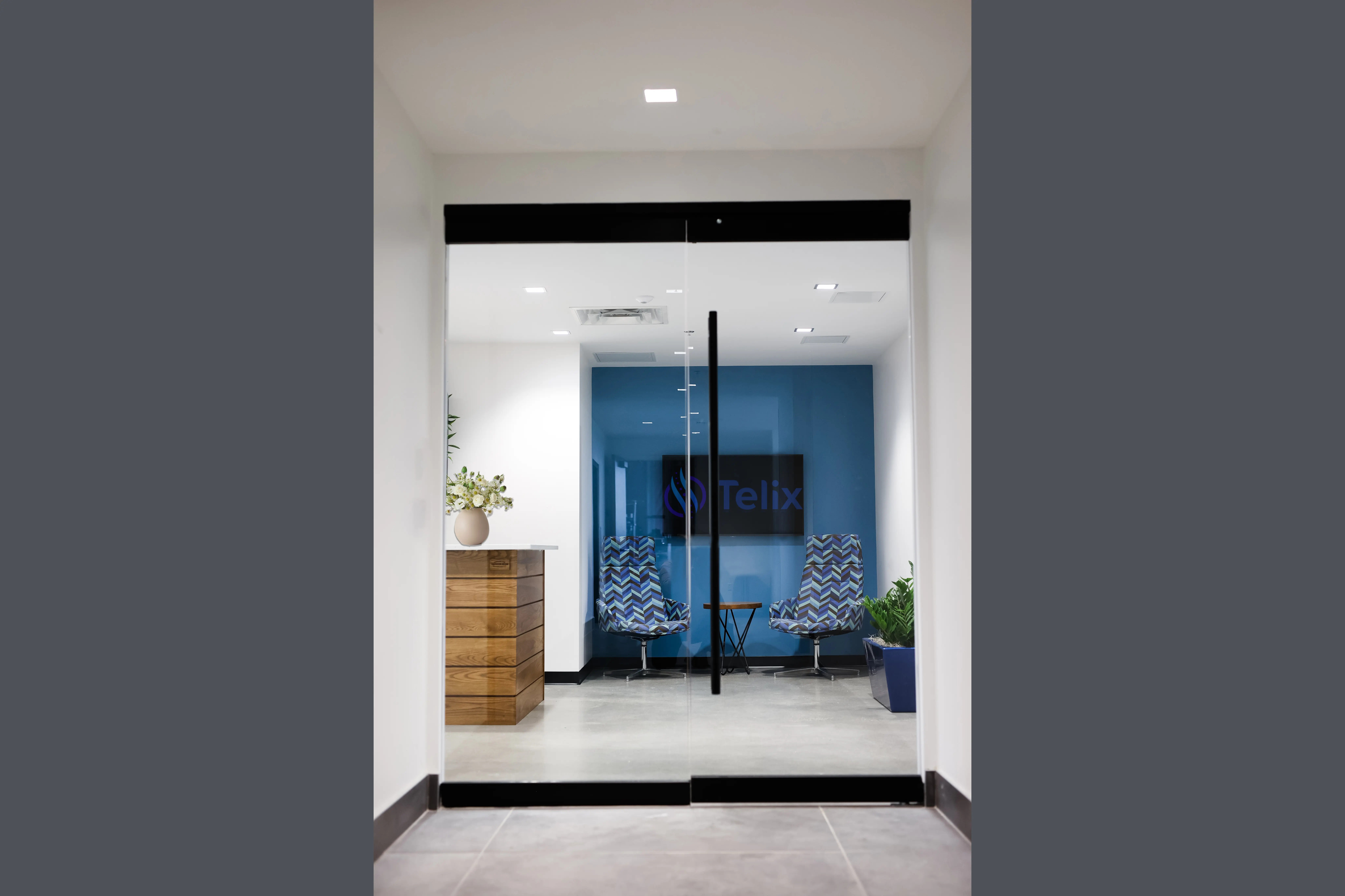 Glass entry to office lounge in Fishers Indiana with modern seating, blue accent wall, and branded Telix interior design