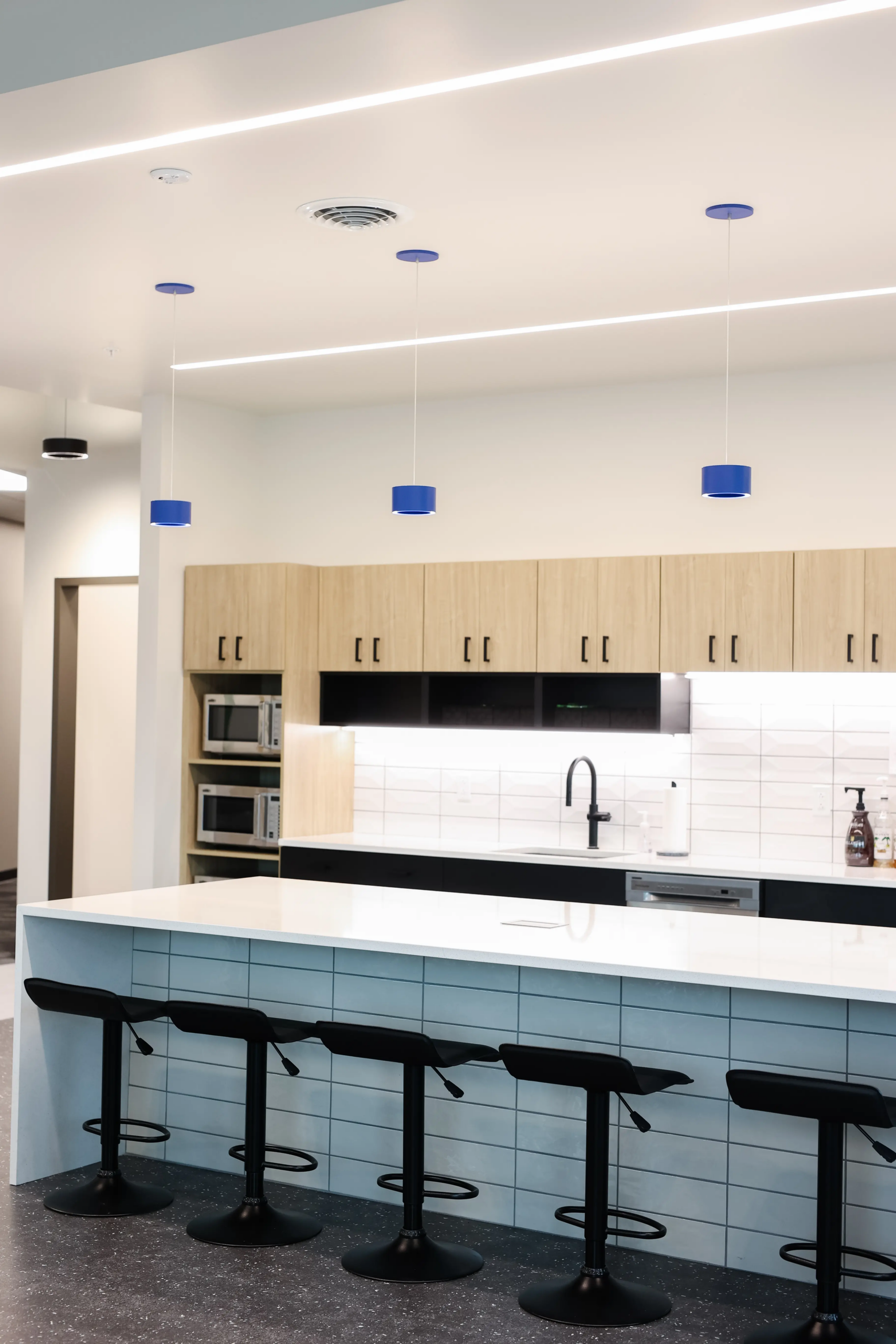 Office breakroom design in Indianapolis with large island seating, pendant lighting, and modern finishes