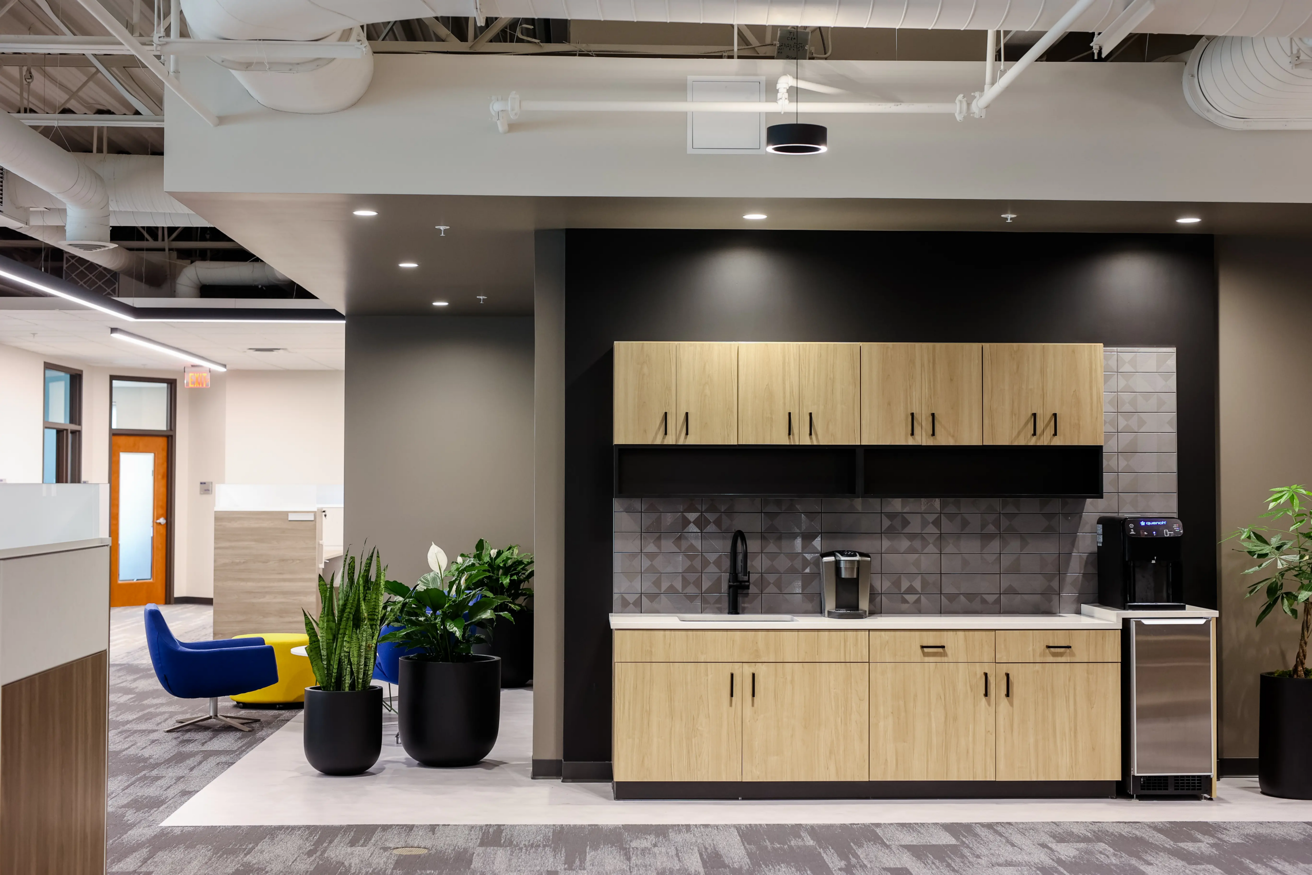 Modern workplace kitchenette with coffee bar, wood cabinetry, and tile backsplash in commercial interior project
