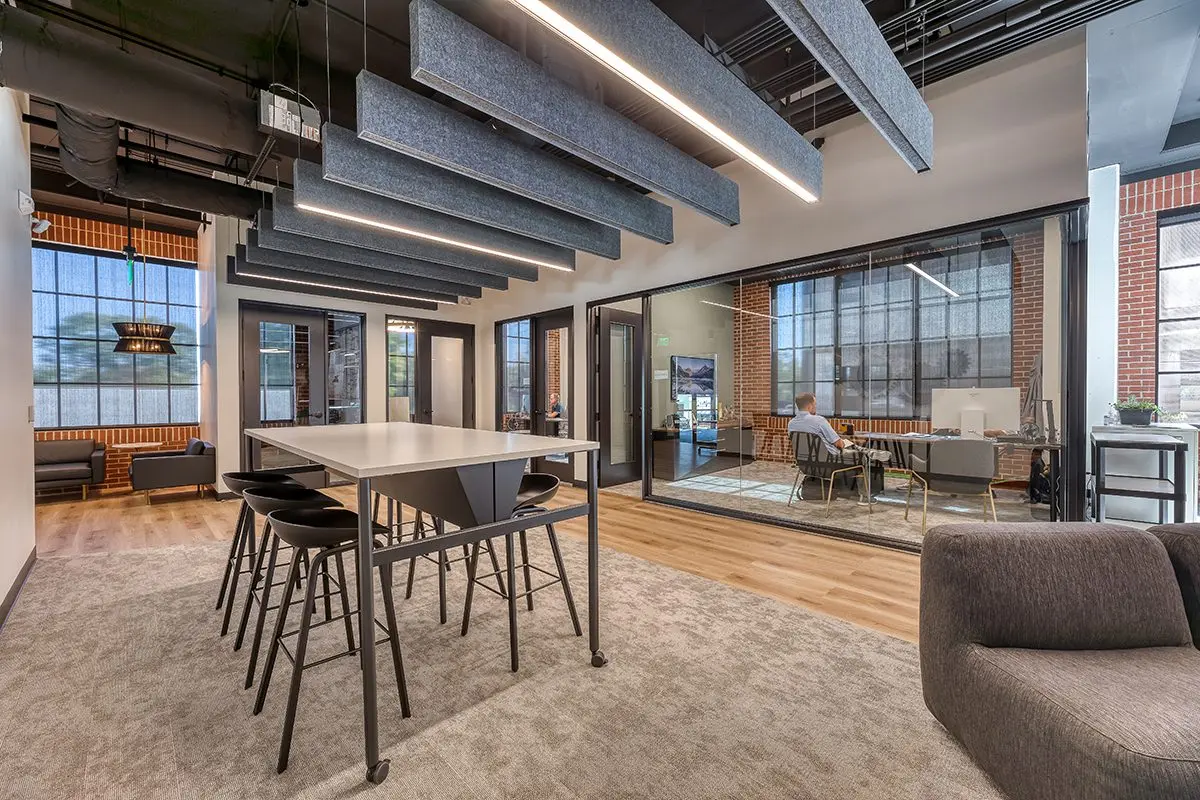 Collaborative office workspace in northern Indiana with shared table, acoustic ceiling panels, and glass meeting rooms