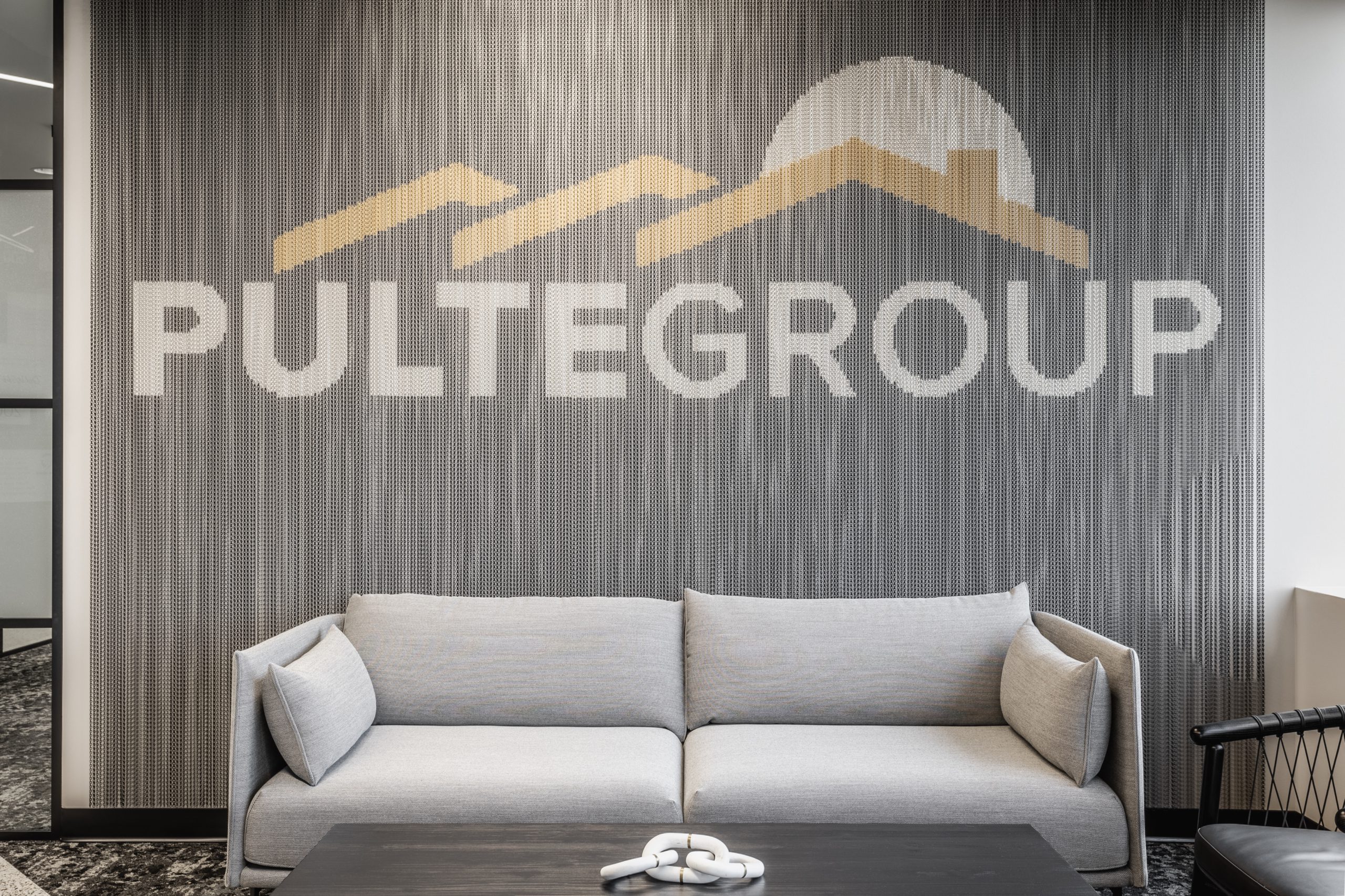 Office lobby seating area with PulteGroup branding wall and modern sofa in Carmel, Indiana workplace design