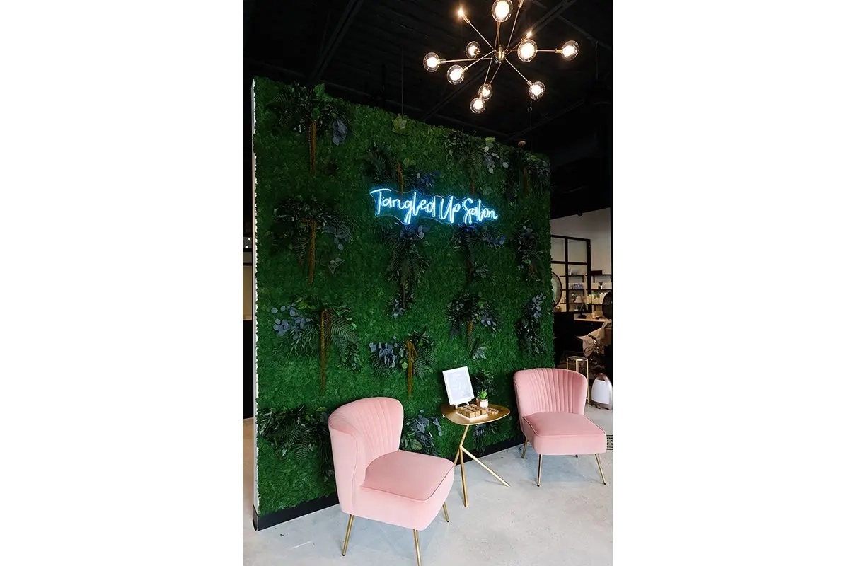 Salon interior in Carmel, Indiana with greenery feature wall, neon signage, and lounge seating